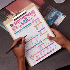Op de afbeelding: Een houten clipboard met een gedrukt borstvoedingslogboek. Het logboek bevat kleurrijke illustraties en secties voor het bijhouden van voedingstijden, signalen van de baby en meer. De tekst "BREASTFEEDING LOG" staat prominent bovenaan.