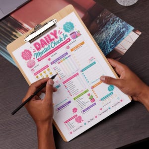 May include: A wooden clipboard holds a "Daily Mental Check-In" sheet with colorful graphics and sections for tracking mood, thoughts, and goals. A black pen is poised to write on the sheet, promoting self-care and mindfulness.