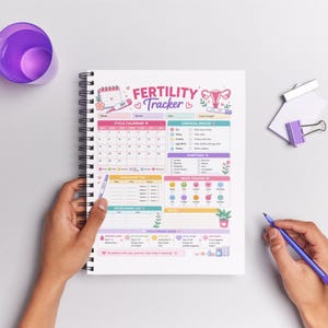 Op de afbeelding: Een spiraalgebonden vruchtbaarheidstracker-notitieboek met een kleurrijk ontwerp. De omslag toont de tekst "Fertility Tracker" en een kalenderindeling. Het notitieboek bevat secties voor cyclusregistratie, ovulatietests en stemmingsregistratie.
