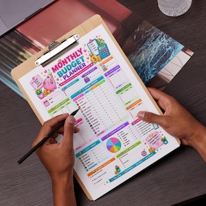 May include: A monthly budget planner sheet on a wooden clipboard featuring a pink piggy bank illustration, a colorful pie chart, and sections for income, expenses, and savings goals with text including Monthly Budget Planner.