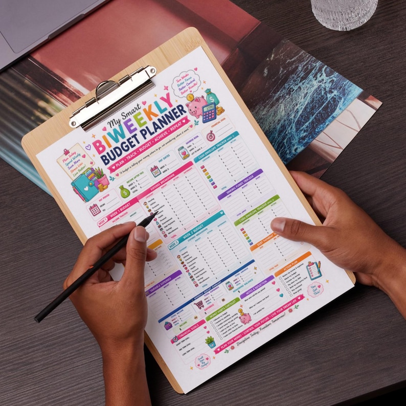 May include: A wooden clipboard holding a printed My Smart Biweekly Budget Planner sheet with colorful graphics, including a pink piggy bank, calculator, and various financial tracking sections for income, expenses, and savings goals.