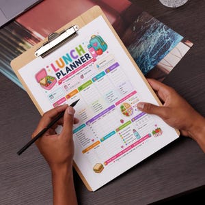 May include: A wooden clipboard holding a printed lunch planner sheet with colorful graphics of a lunchbox, water bottle, and apple. The planner includes sections for daily meals, water intake, and notes, with the text LUNCH PLANNER at the top.