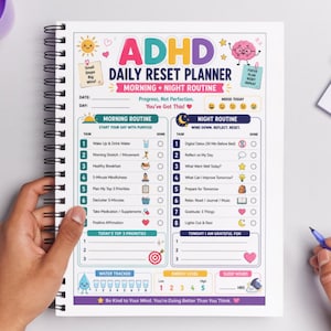 Peut inclure: Un planificateur quotidien de réinitialisation ADHD à spirales avec des sections de routine du matin et du soir. Le planificateur comprend des sections pour les tâches, le suivi de l'eau et les niveaux d'énergie. Le texte "ADHD" et "Daily Reset Planner".