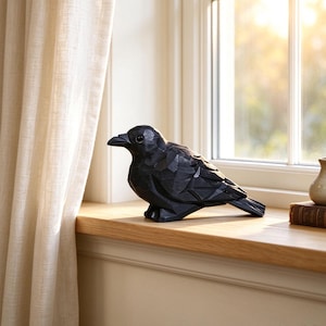 May include: A black bird figurine with a faceted, geometric surface texture. The sculpture features a sharp beak, a smooth eye, and a stylised wing design, capturing the form of a crow or raven in a solid, dark, matte finish.