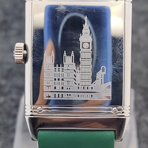 May include: A rectangular silver wristwatch with a green leather band. The watch face features an etched image of the Big Ben clock tower and other buildings. The watch has a silver crown and a green leather strap.