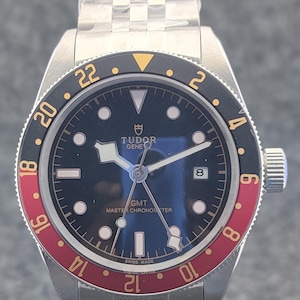 Puede incluir: Una taza de cerámica blanca con un asa negra y el texto "But First, Coffee" en negrita negra. La taza se encuentra sobre un fondo neutro, resaltando su diseño sencillo.