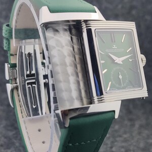 May include: A rectangular wristwatch with a green face and a green leather band. The watch has silver-colored accents and a small seconds dial. The band is stitched with white thread and has a silver clasp.