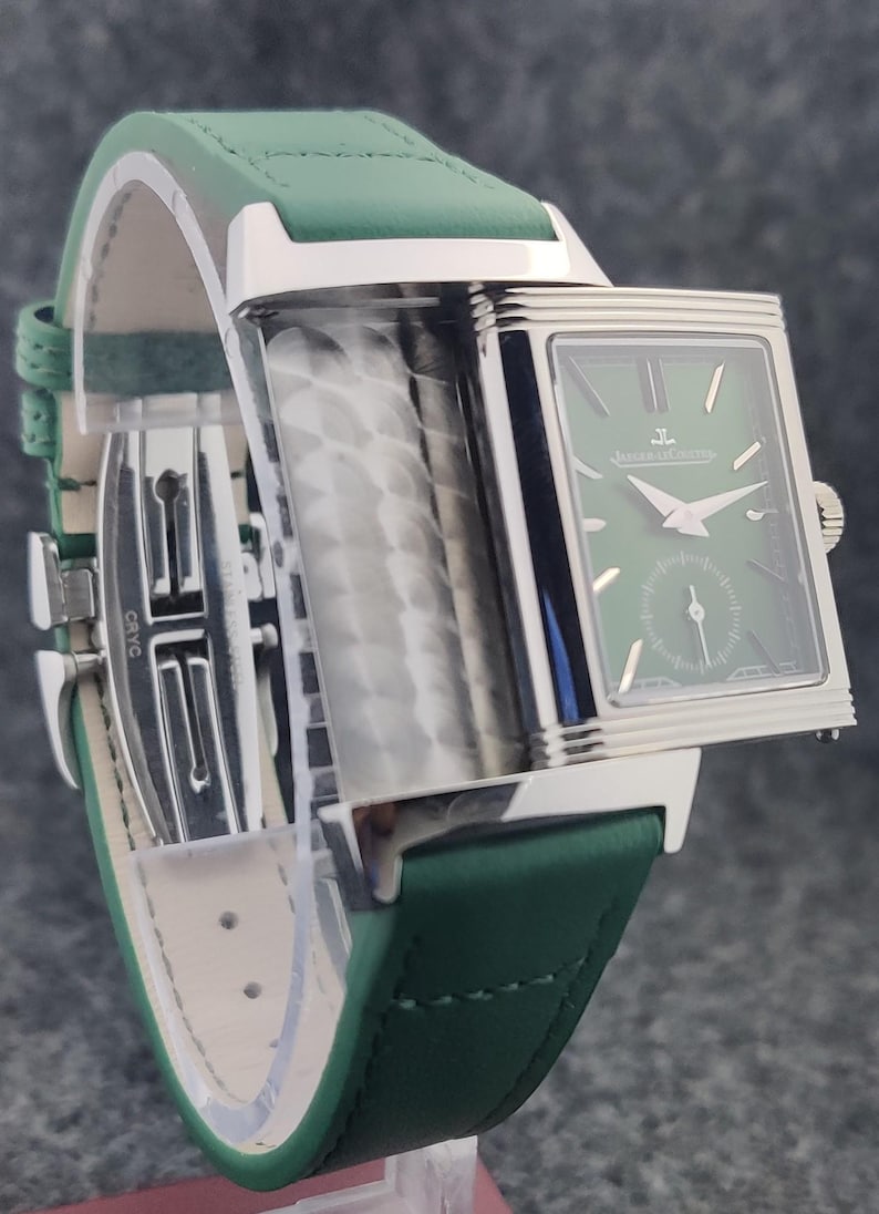May include: A rectangular wristwatch with a green face and a green leather band. The watch has silver-colored accents and a small seconds dial. The band is stitched with white thread and has a silver clasp.