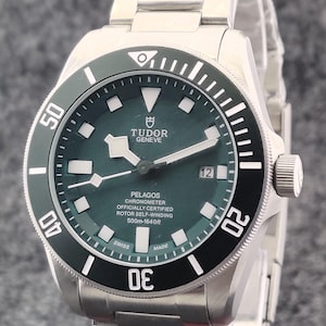 May include: A stainless steel Tudor Pelagos watch with a dark green dial and a black rotating bezel. The watch face displays the text "TUDOR GENEVE PELAGOS CHRONOMETER" and "500m-1640ft". The watch has a date display at the 3 o'clock position.