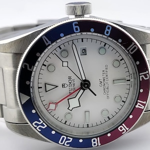 May include: A stainless steel wristwatch with a white dial, black hands, and a date window at the 3 o'clock position. The bezel is colored in blue, black, and burgundy. The watch has a stainless steel band.