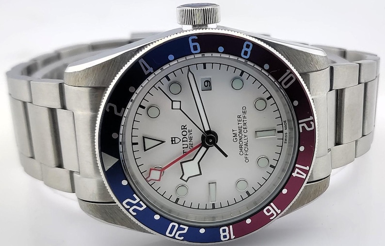 May include: A stainless steel wristwatch with a white dial, black hands, and a date window at the 3 o'clock position. The bezel is colored in blue, black, and burgundy. The watch has a stainless steel band.
