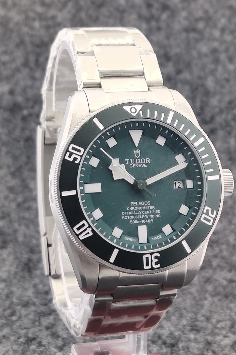 May include: A stainless steel Tudor Pelagos watch with a dark green dial and a black rotating bezel. The watch features luminous markers, a date display, and a stainless steel bracelet. The dial reads "PELAGOS CHRONOMETER" and "500m-1640ft".