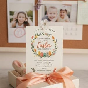 Op de afbeelding: Een paasuitnodigingskaart met de tekst "You're Invited" en "Hop on Over to Our Easter Celebration". De kaart is versierd met een bloemenkrans en pastelkleurige eieren. Een geschenkdoos met een perzikkleurig lint en een "Happy Easter"-label staat ervoor.