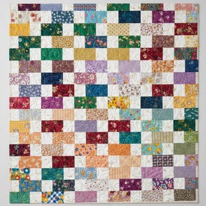 Könnte beinhalten: Ein Patchwork-Quilt mit einem Rastermuster. Der Quilt zeigt eine Vielzahl von Stoffquadraten in einer Mischung aus Farben und Mustern, darunter Blumenmuster, Streifen und unifarbene Farben. Die Quadrate sind in einem Schachbrettmuster mit weißen Quadraten angeordnet.