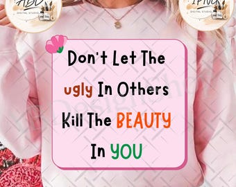 May include: A light pink sweatshirt featuring a rectangular graphic with a pink flower and the text: Don't Let The ugly In Others Kill The BEAUTY In YOU. The word ugly is in brown, BEAUTY is in orange, and YOU is in green, with black text.