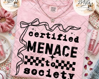 May include: A light pink t-shirt featuring a black graphic print with a ribbon bow at the top and the text "certified MENACE to society" in a distressed font. The design includes a checkered pattern and small star accents, with a silver butterfly necklace.