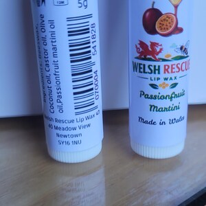 May include: Two white lip balm tubes. One has a label with a passionfruit martini design and the text "WELSH RESCUE LIP WAX Passionfruit Martini Made in Wales". The other tube has the text "Net: 5g" and ingredient information.