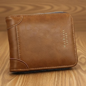 Puede incluir: Una cartera de cuero marrón con cierre de cremallera. La cartera tiene el texto "Men Bense Leather" grabado en relieve en la parte delantera. La cartera está sobre una superficie de madera.