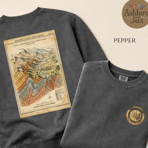 Può includere: Una felpa girocollo grigio antracite con una grande illustrazione vintage di una sezione geologica dell'Elk Range sul retro e un piccolo grafico circolare a bussola sul petto. Il tessuto presenta un aspetto slavato e sbiadito.