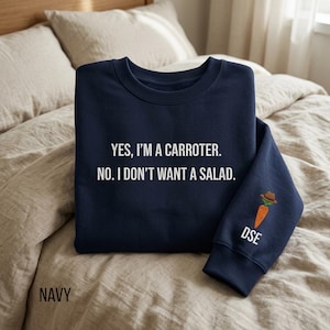 May include: Navy blue sweatshirt with the text "YES, I'M A CARROTER. NO. I DON'T WANT A SALAD." A carrot wearing a hat is on the sleeve, with the initials "DSE" below. The word "NAVY" is at the bottom.
