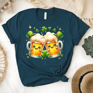 Peut inclure: T-shirt bleu marine avec un motif de la Saint-Patrick. Le graphisme repr&eacute;sente deux chopes de bi&egrave;re de dessin anim&eacute; qui s'entrechoquent, chacune avec un chapeau de lutin vert et un visage souriant. Des tr&egrave;fles et des &eacute;toiles verts sont dispers&eacute;s.