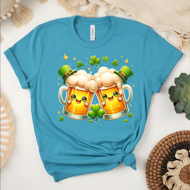 Peut inclure: Un t-shirt turquoise avec un motif de la Saint-Patrick. Le graphisme repr&eacute;sente deux chopes de bi&egrave;re de dessin anim&eacute; avec des visages souriants, de la mousse et des chapeaux de lutin verts. Des tr&egrave;fles verts et des &eacute;toiles dor&eacute;es sont dispers&eacute;s autour des chopes.
