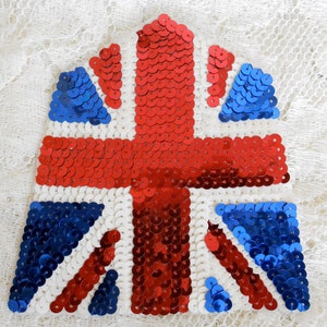 May include: A sequined Union Jack patch in red, white, and blue. The design features the cross of St. George, the saltire of St. Patrick, and the crosses of St. Andrew. The sequins are sewn onto a white fabric base, creating a shimmering effect.