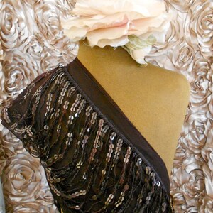 May include: A dark brown, sequined shoulder wrap draped over a mannequin. The wrap features rows of silver sequins and a dark brown trim. A large, light pink and cream fabric flower adorns the mannequin's head, set against a backdrop of fabric roses.