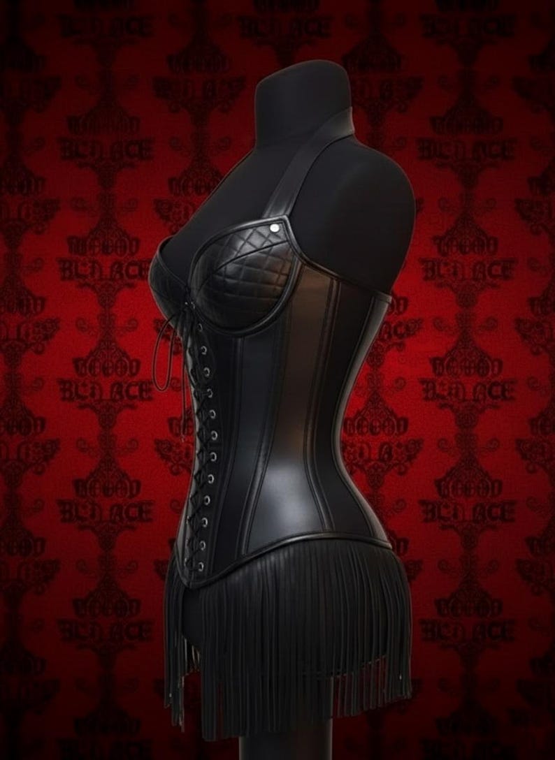 May include: Black leather corset with a halter neck and fringe detail. The corset features a quilted bust and a lace-up back. The garment is displayed on a black mannequin against a red patterned background.