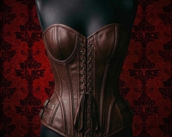 May include: A brown leather corset with a sweetheart neckline and a lace-up back. The corset features vertical seams, decorative buckles, and is displayed on a black mannequin. The background is a red damask pattern.