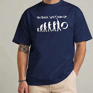 Puede incluir: Camiseta azul marino con texto blanco y un gráfico que representa la evolución humana, que termina con un círculo. El texto sobre el gráfico dice "Go Back, We F*cked Up."