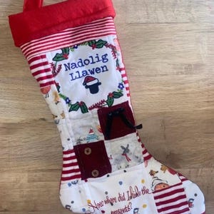 May include: A patchwork Christmas stocking featuring red and white striped fabric, a white panel with the embroidered text Nadolig Llawen, a small black hat icon, and the text Now where did I hide the presents? with various small fabric squares.