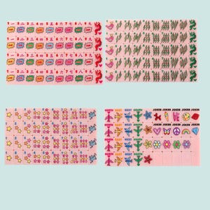 Pu&ograve; includere: Un set di tessere per mahjong rosa con varie grafiche colorate tra cui numeri, caratteri cinesi, fulmini, uccelli, stelle, aerei, fiori, cuori, arcobaleni e la parola JOKER stampata su tessere specifiche disposte in una griglia.