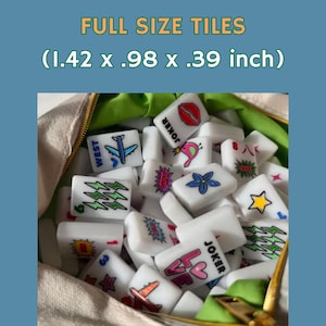 Pu&ograve; includere: Una collezione di tessere rettangolari bianche con stampe grafiche colorate tra cui fulmini, fiori, stelle, labbra e la parola JOKER, che misurano 3,61 x 2,49 x 0,99 cm, contenute in un sacchetto di tessuto beige con fodera verde.