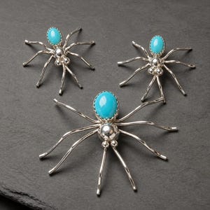 May include: Three spider-shaped brooches crafted from polished silver metal. Each spider features a smooth, oval-shaped turquoise gemstone as the body, with slender, curved silver legs extending outward from a central rounded silver segment.