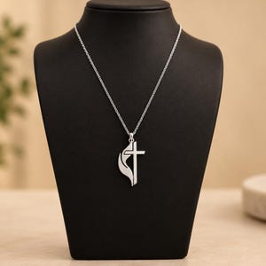 May include: A silver-toned necklace featuring a pendant that combines a traditional cross shape with a stylized flame element on the left side, suspended from a delicate silver-toned chain link necklace.
