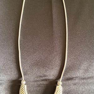 May include: Silver-toned necklace with a geometric pendant. The necklace features a chain and a central pendant composed of three connected shapes. The shapes have a textured, striped design.