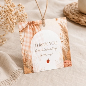 May include: A square paper gift tag with a hole at the top and a jute string. The tag features a beige gingham bow, dried pampas grass, and a white arch. It displays the text THANK YOU for celebrating with us! and a small red mug icon.