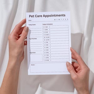 May include: A white printed paper titled "Pet Care Appointments" is held by two hands. The paper includes sections for "Today Goals," "Top Priorities," and "Today's Schedule" with time slots from 6 AM to 9 PM. The text is in black.