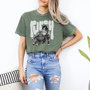 May include: Olive green t-shirt with the word "FUNKY" in white, above a black and white graphic of two monkeys. The shirt is a relaxed fit and has short sleeves.