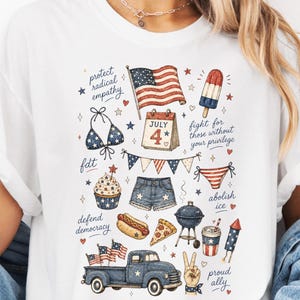 May include: White t-shirt with a patriotic illustration featuring an American flag, July 4th calendar, bikini, shorts, cupcake, hot dog, pizza, truck, and other festive elements. The shirt has text that says "protect radical empathy", "defend democracy", and "abolish ice".