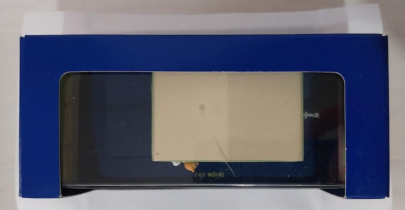 Puede incluir: Una caja rectangular azul con una ventana transparente, que revela un producto en su interior. La caja tiene un interior blanco y un exterior azul oscuro. El texto "CILE NOIRE" es visible en el producto.