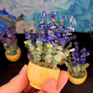 May include: A small decorative tree sculpture in a yellow ceramic pot, featuring wire branches adorned with tumbled green and blue gemstone chips. The sculpture mimics a flowering plant with light green stones at the base and deep blue stones at the top.