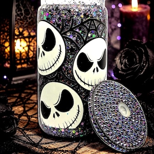 May include: A clear glass tumbler with a black and white Jack Skellington design and a matching lid. The tumbler is filled with glitter and has a black spiderweb design. The lid is covered in iridescent rhinestones. Halloween themed.
