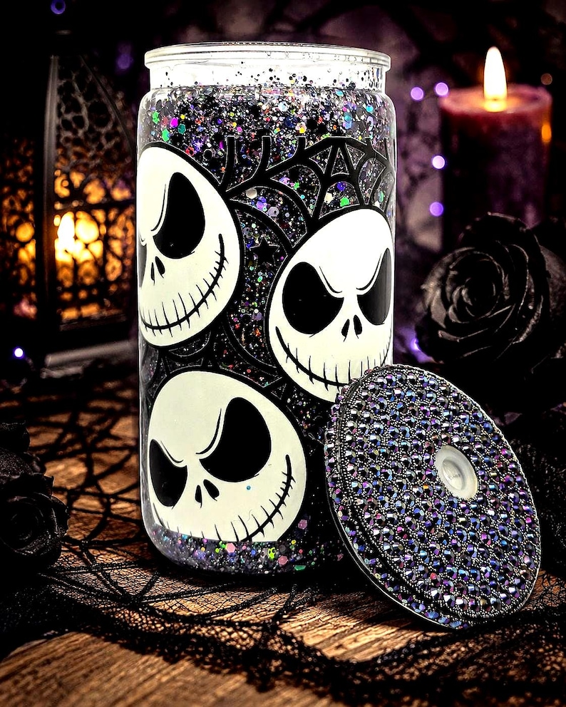 May include: A clear glass tumbler with a black and white Jack Skellington design and a matching lid. The tumbler is filled with glitter and has a black spiderweb design. The lid is covered in iridescent rhinestones. Halloween themed.