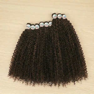 May include: Dark brown curly hair extensions bundles. The bundles are labeled with numbers 60, 65, and 70. The hair is arranged in a wavy pattern on a light wood surface.