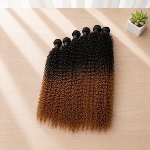 Puede incluir: Un paquete de extensiones de cabello con una textura de rizos apretados y encrespados. El cabello pasa de un color negro intenso en la parte superior cerca de la trama a un tono marrón medio cálido en las puntas, creando un efecto degradado.