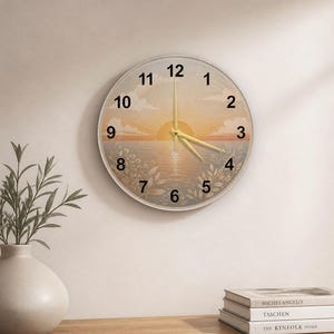 May include: Round wall clock with a sunset scene. The clock face features a sunrise over water with floral accents. The clock has gold-colored hands and a white frame. Numbers 1 through 12 are displayed around the clock face.