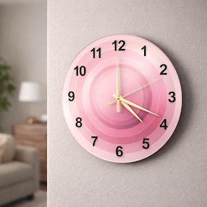 May include: A round wall clock with a pink gradient design. The clock face features concentric circles of varying shades of pink, with black numerals marking the hours. The clock hands are gold-colored.