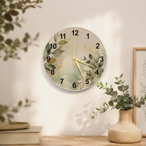 May include: A round wall clock featuring a watercolor-style design with green leaves and gold accents on a cream background. The clock face displays black numerals from 1 to 12 and includes thin, gold-colored hour, minute, and second hands.